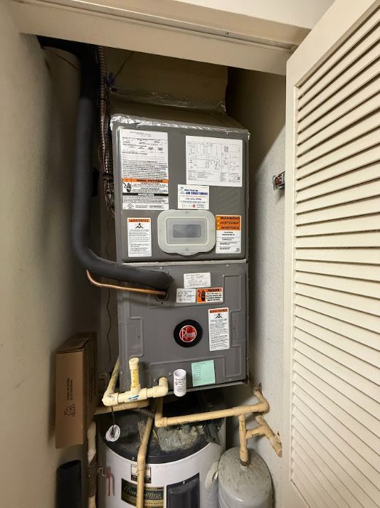 Water heater and HVAC unit in a narrow utility closet with white louvered doors.