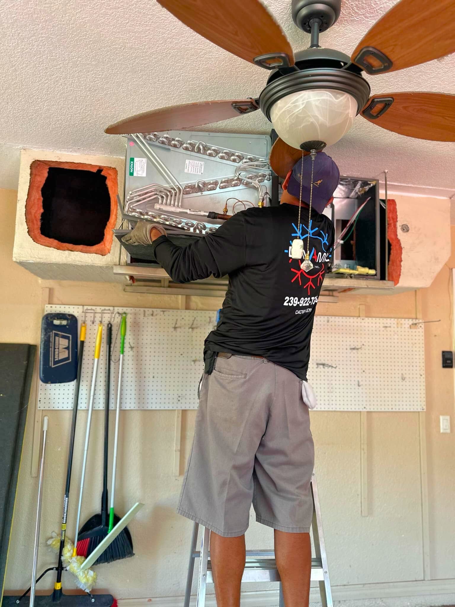 Person installing a ceiling fan in a garage with tools and pegboards on the wall
