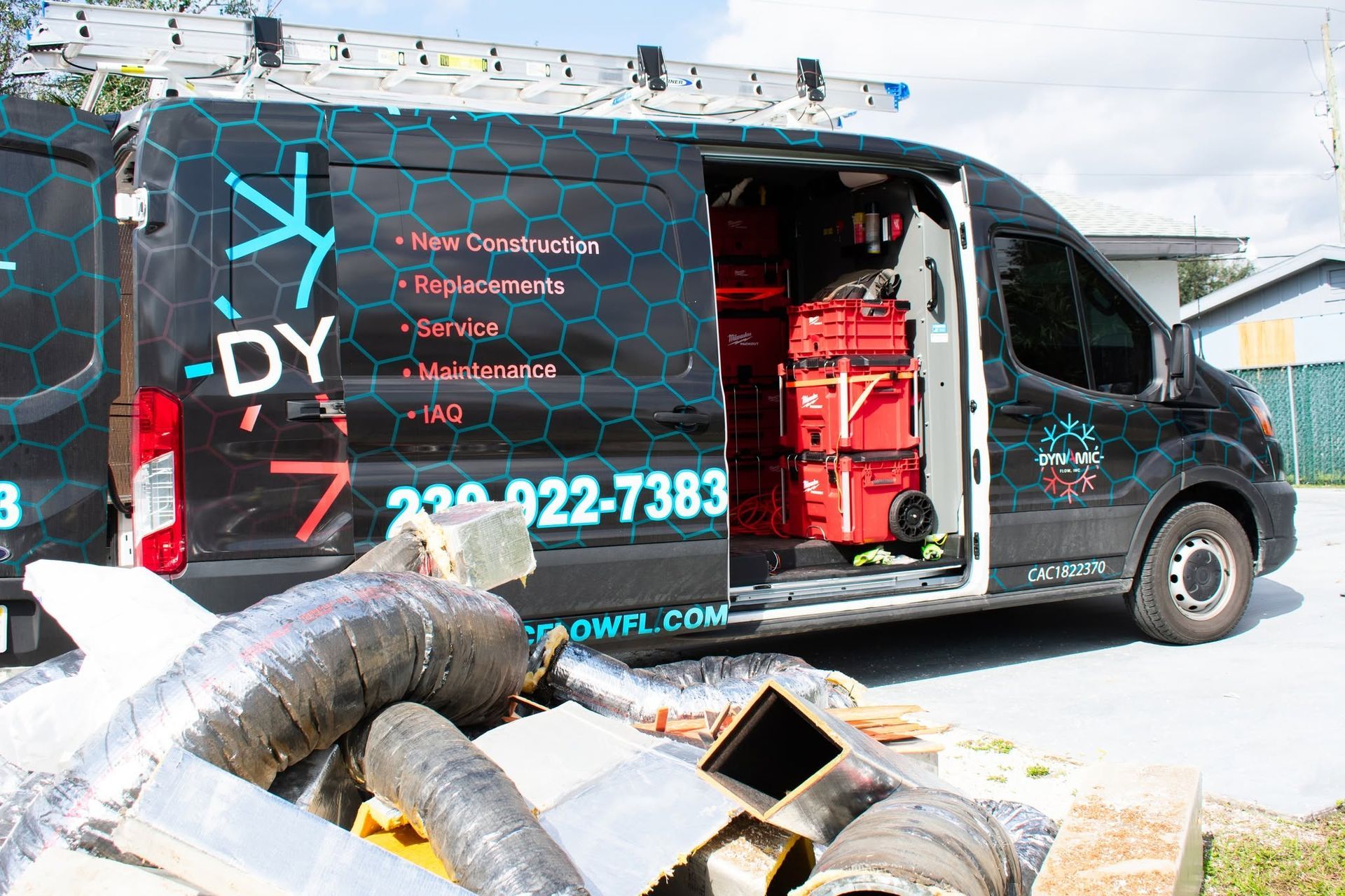 Black service van with open side door, showing red equipment inside, parked beside storm debris and ductwork