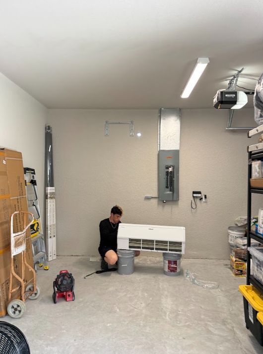 Person kneeling in a garage beside a white cabinet, with tools and boxes around them