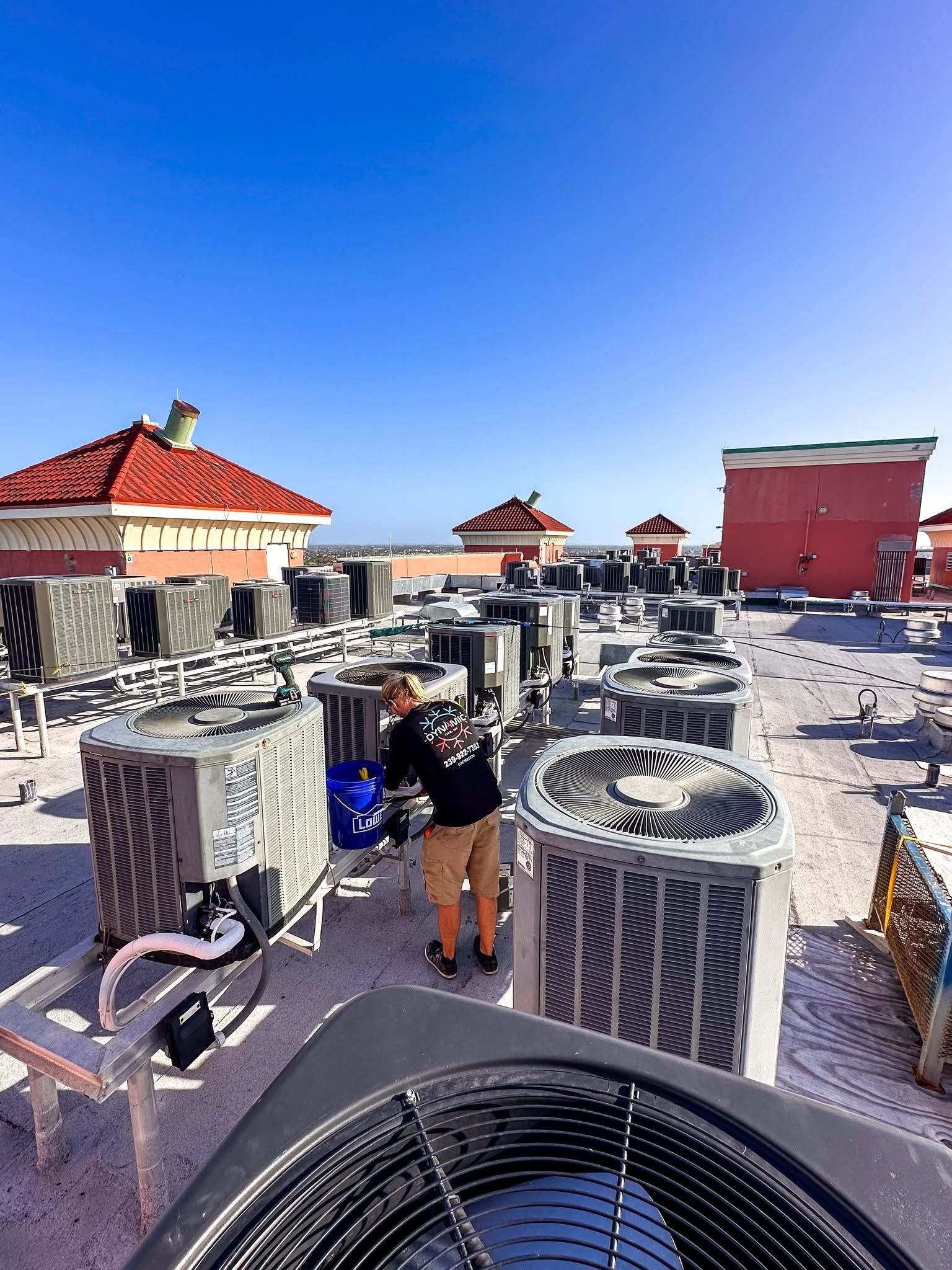 Rooftop HVAC units under a clear blue sky, with red-roofed buildings in the background.