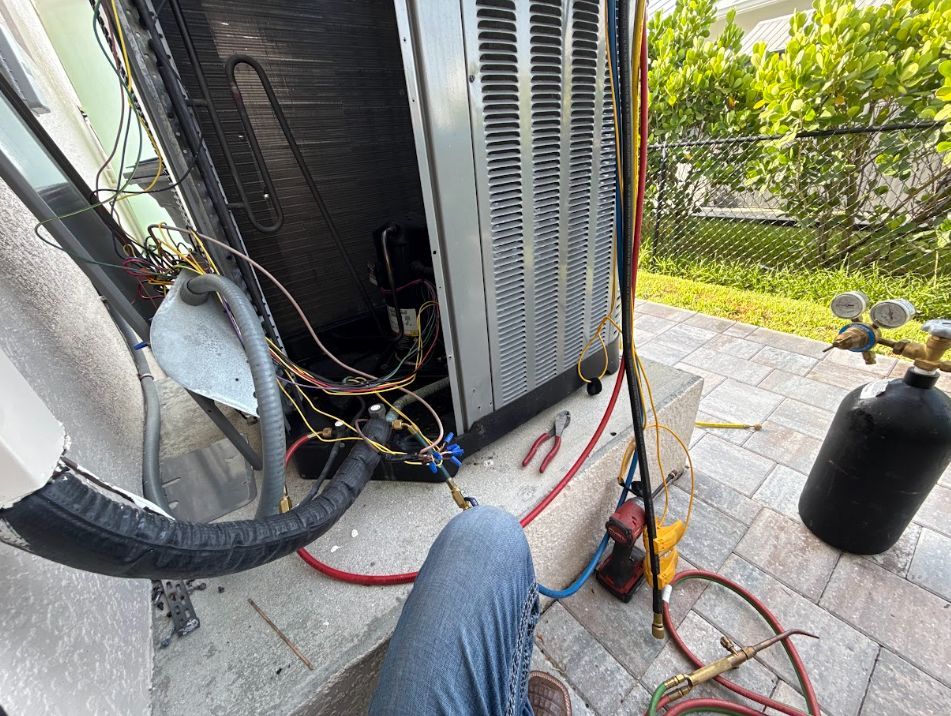 HVAC unit with gauges and hoses connected, sitting on a patio beside a yard.