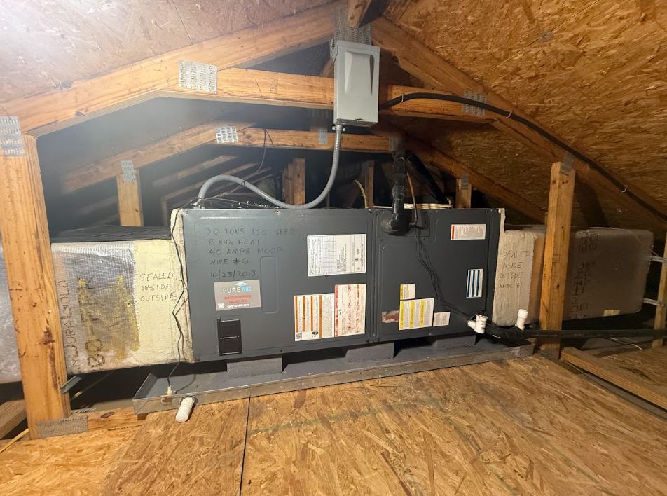 Attic HVAC unit and ductwork under a sloped roof with exposed insulation and wiring