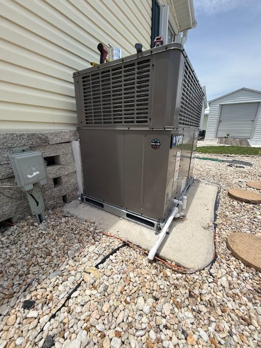 Outdoor HVAC unit beside a house, sitting on a concrete pad with gravel around it