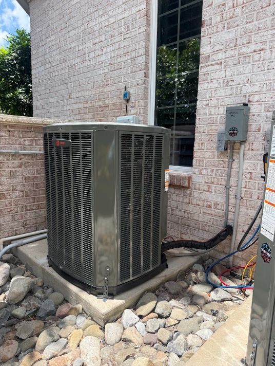 Outdoor air conditioner unit beside a brick building, with gravel and electrical equipment nearby
