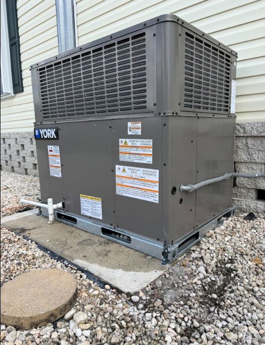 York HVAC unit beside a house, sitting on gravel next to a stone foundation and siding