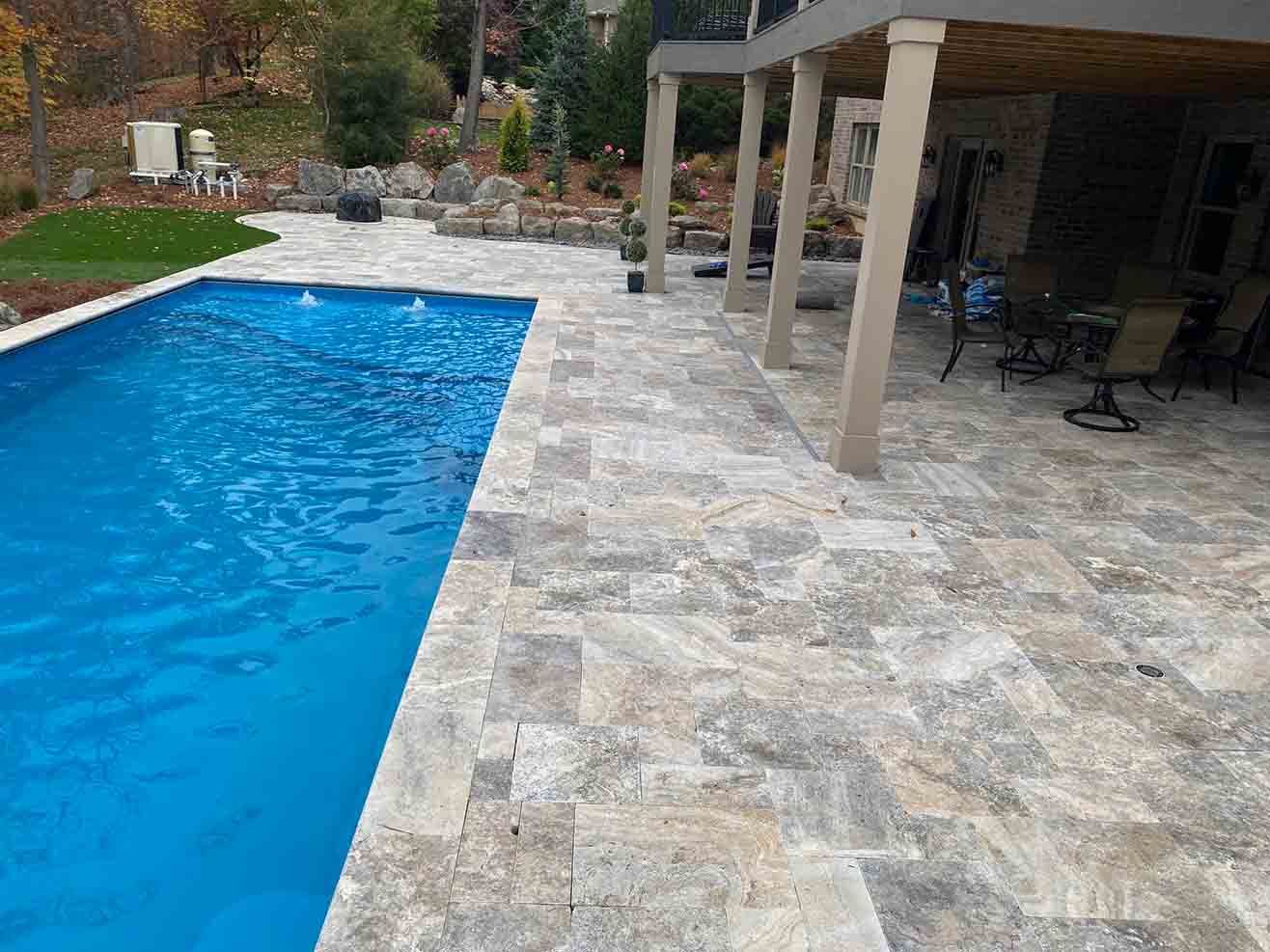 Silver travertine pool deck laid in a patterned set around a backyard pool