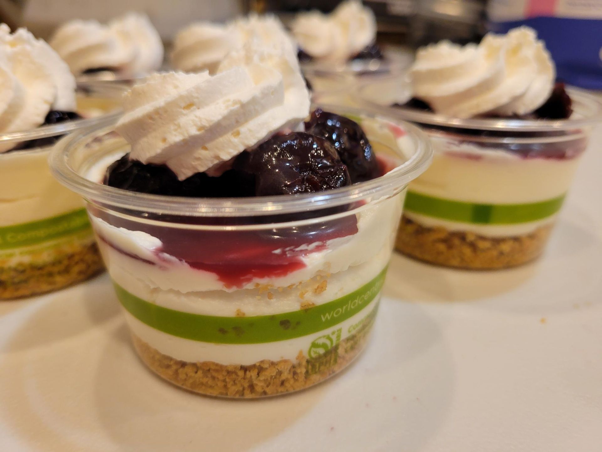 Dessert cups with layered cream, green filling, berry topping, and whipped cream, arranged in rows