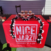 Red dessert display table with jars and a red NICE JARZ! tablecloth outdoors