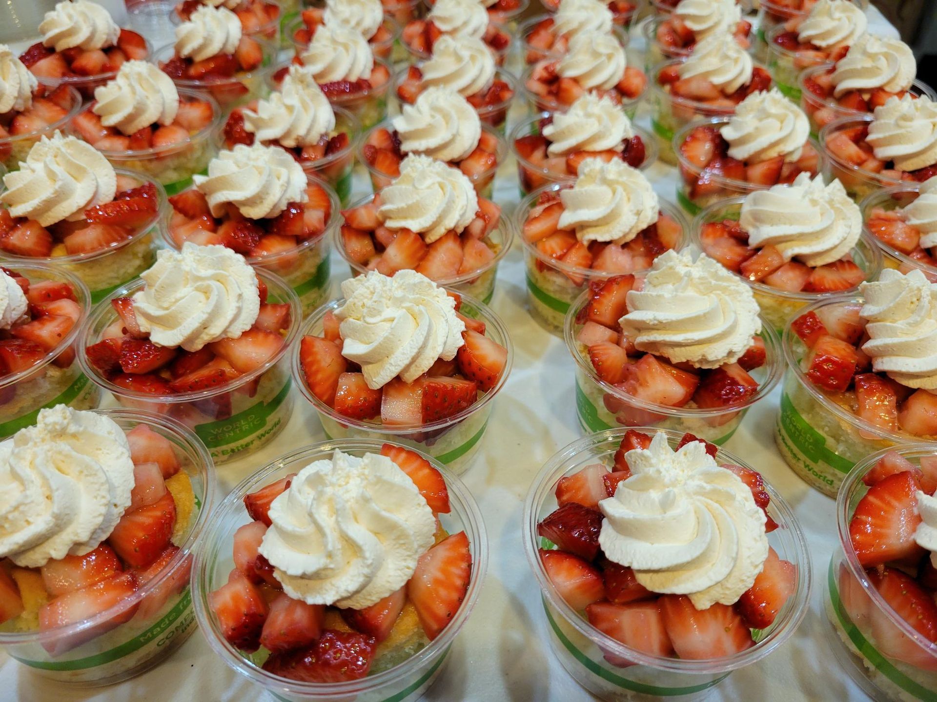 Rows of strawberry dessert cups topped with whipped cream on a tray