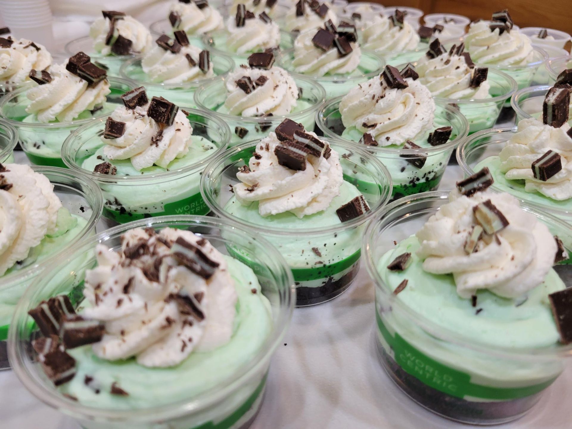 Rows of green-tinted dessert cups topped with whipped cream and chocolate shavings