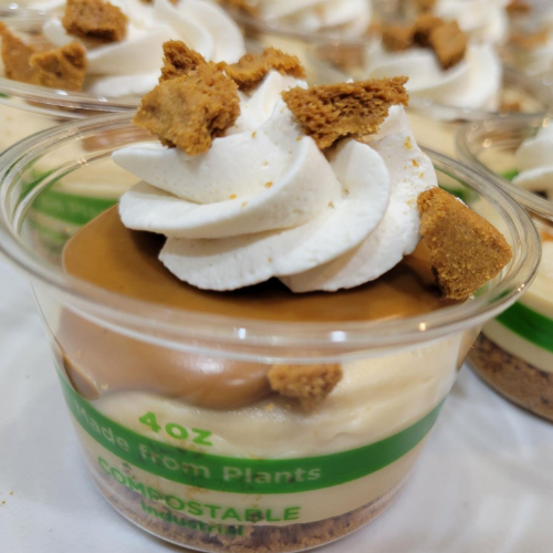 Dessert cups topped with whipped cream and cookie crumbs, with green compostable labels