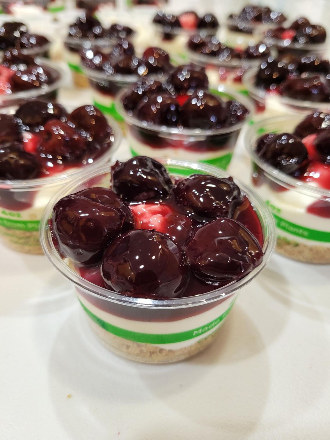 Rows of clear dessert cups topped with dark grapes and red jelly on a white table