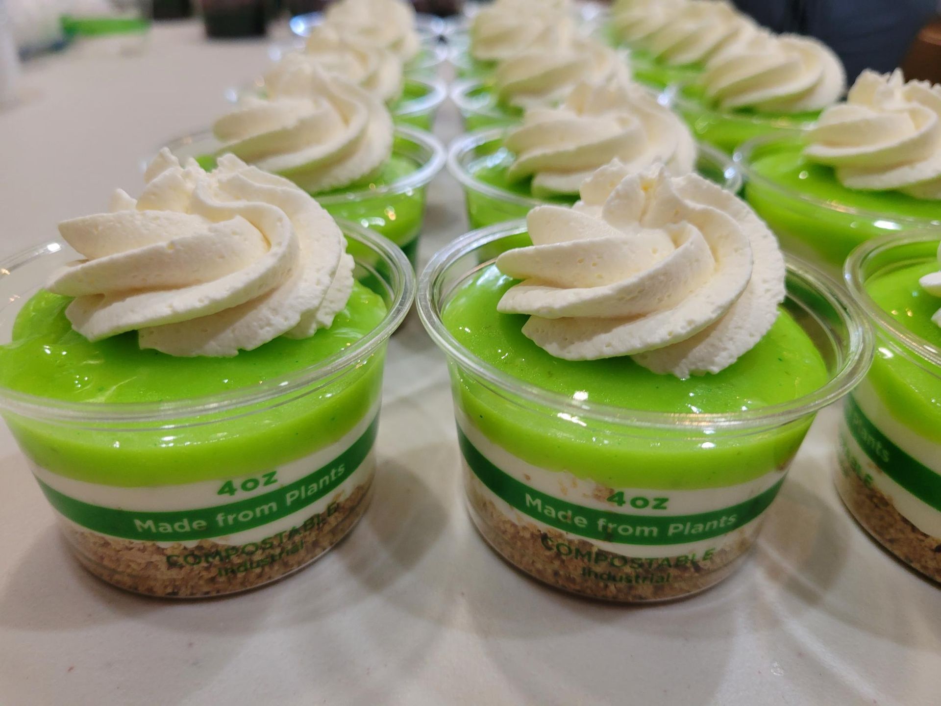 Rows of green layered dessert cups topped with swirled white cream on a table