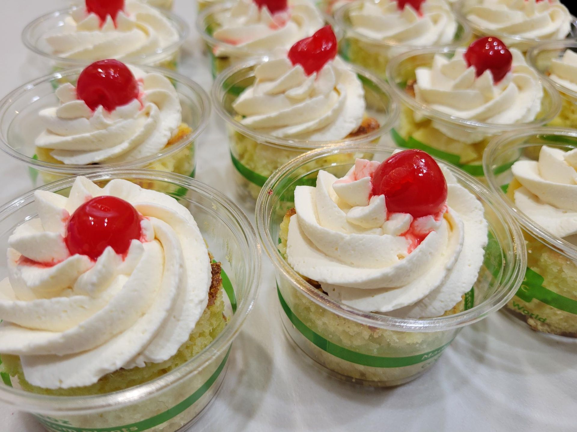 Cup desserts with white whipped cream swirls and red cherries in clear glass cups