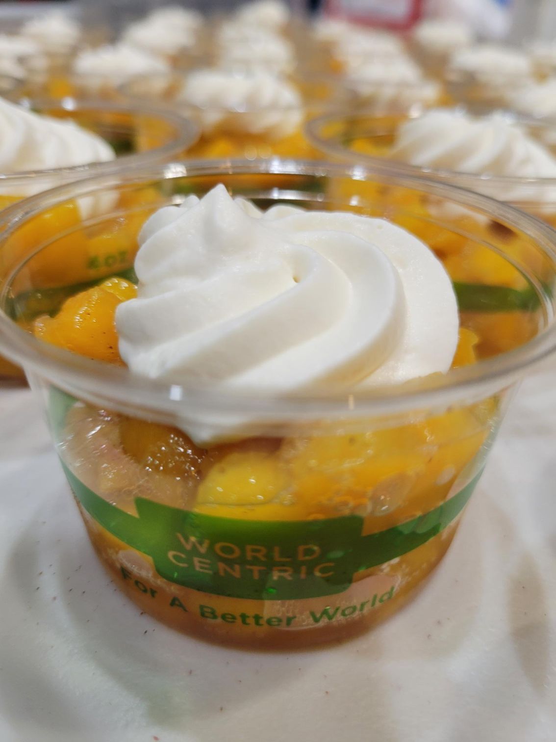 Mini dessert cups with white whipped topping and orange fruit pieces on a tray