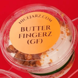 Clear plastic cup of butter fingerz candy labeled “NICEJARZ.COM” on a red surface.