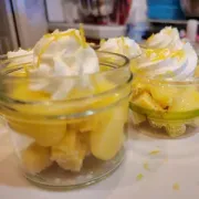 Dessert cups with yellow custard, sponge cake, and whipped cream topped with lemon zest