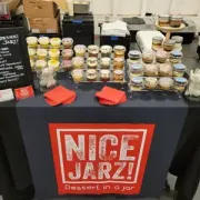 Market stall table with jars of Nice Jarz preserves and two red napkins on a black cloth display