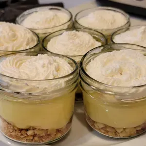 Glass dessert cups layered with crumb crust, yellow custard, and whipped cream on top