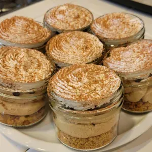 Six glass jars of layered dessert topped with powdered sugar on a white plate.