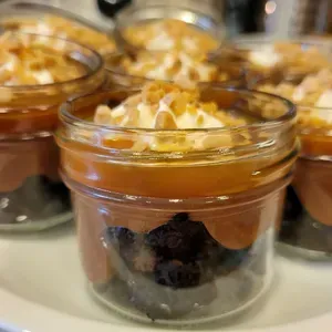 Glass dessert jars with caramel pudding, whipped cream, and nuts on a tray