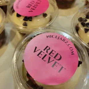 Pink-labeled red velvet dessert cups in clear lids, topped with chocolate chips.