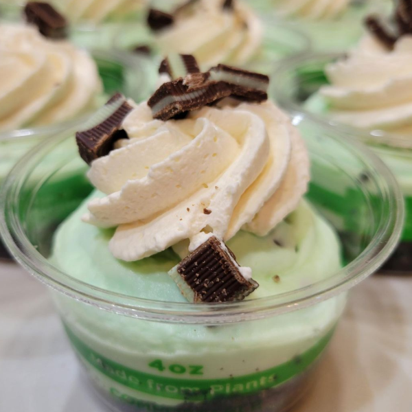 Mint green dessert cups topped with whipped cream and chocolate pieces in clear plastic containers