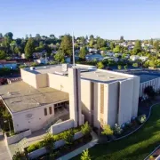 Aerial view of a beige church building with a tall tower in a green suburban neighborhood