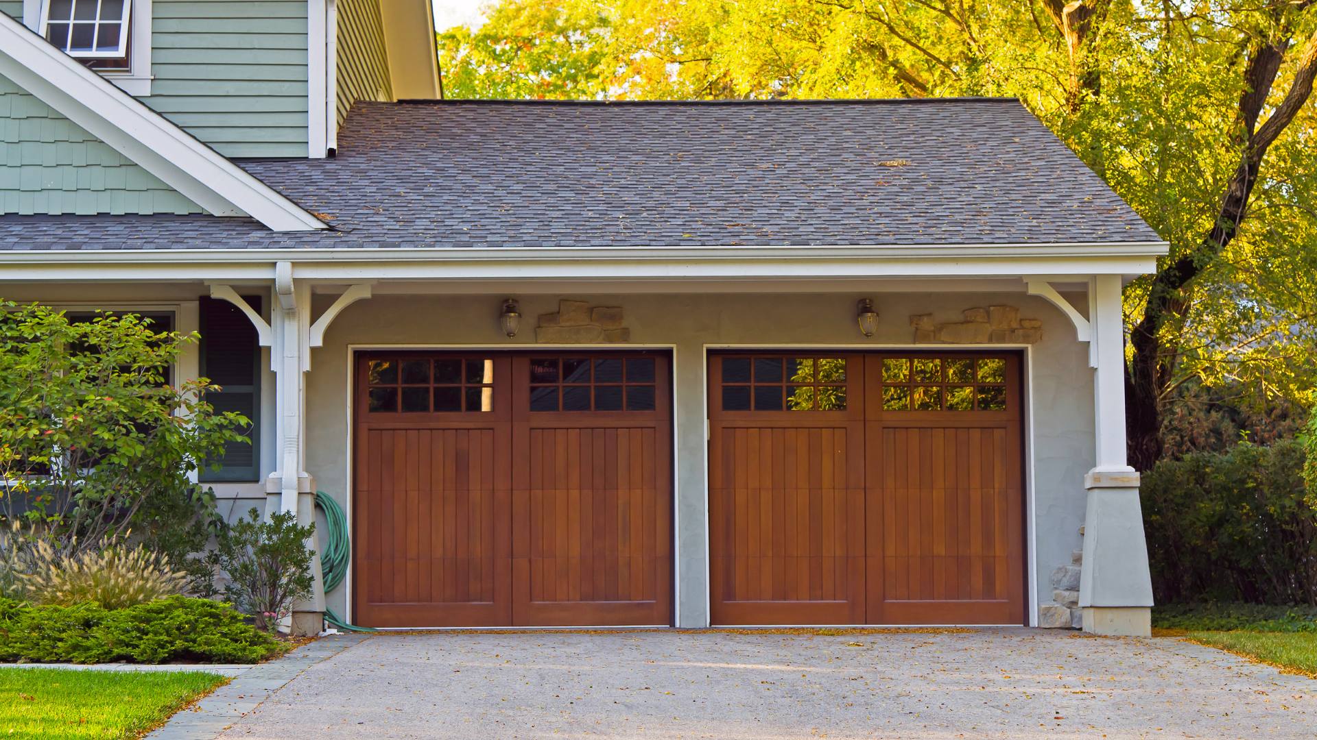 Two-car wooden garage doors on a suburban house with white trim and a gravel driveway