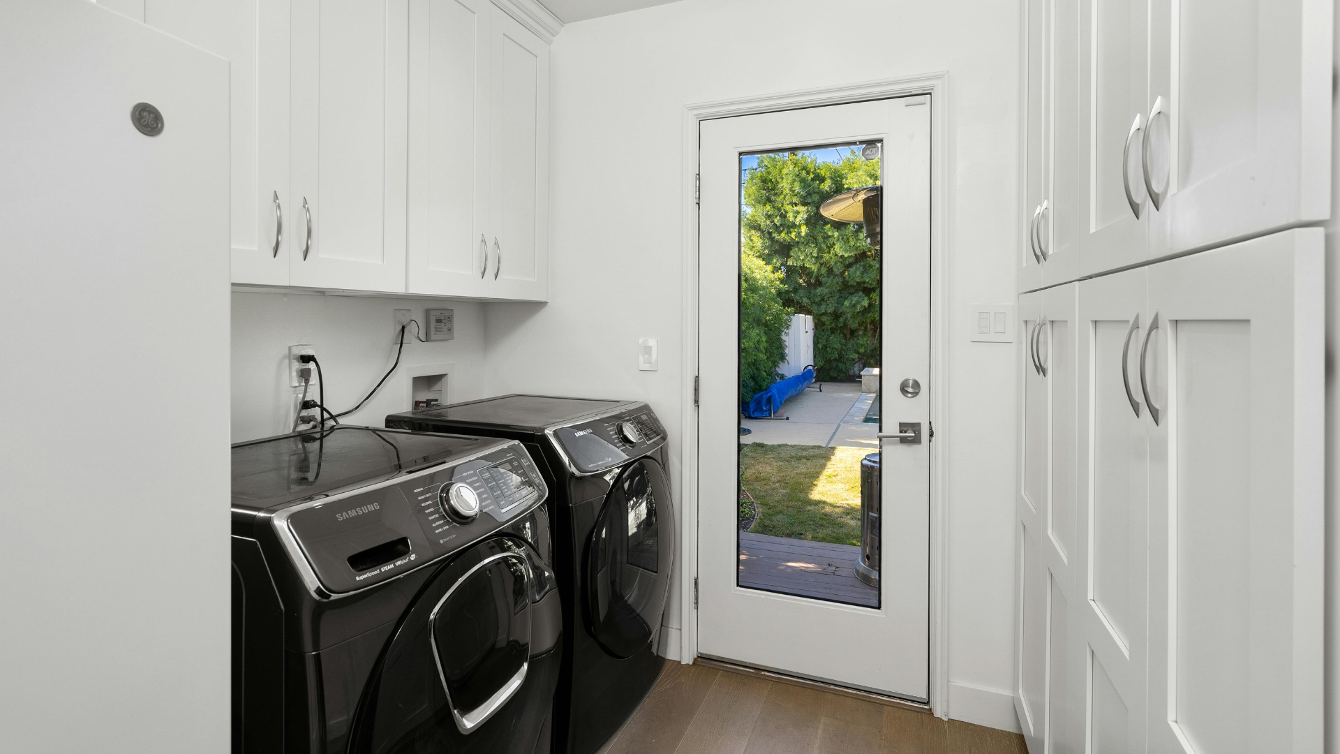 Laundry room with black washer and dryer, white cabinets, and a glass door to a garden outside