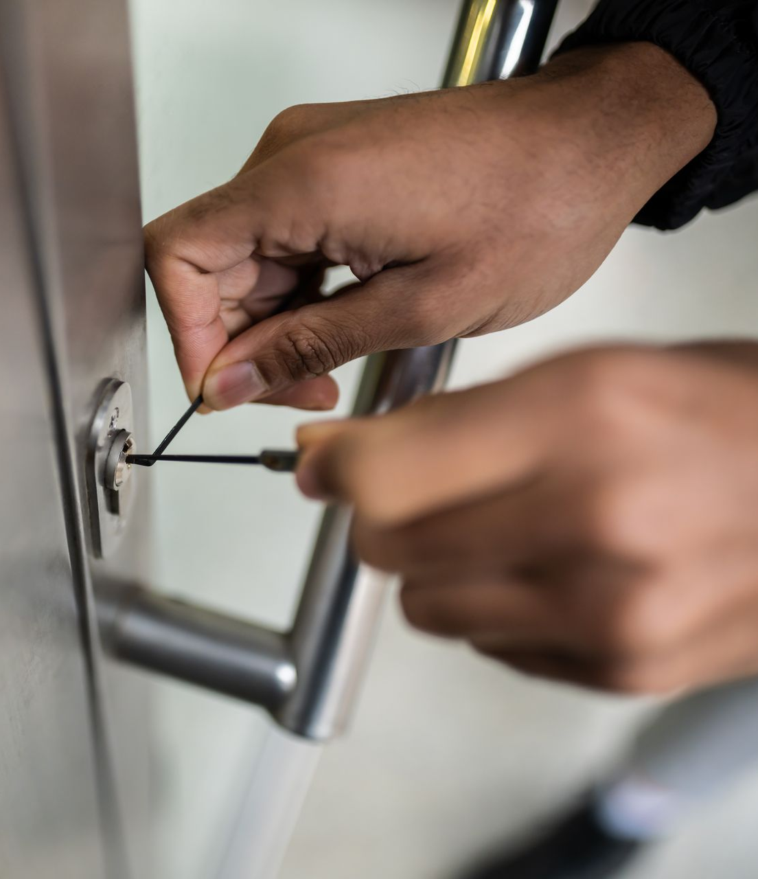 Hands using a key to unlock a metal door handle.