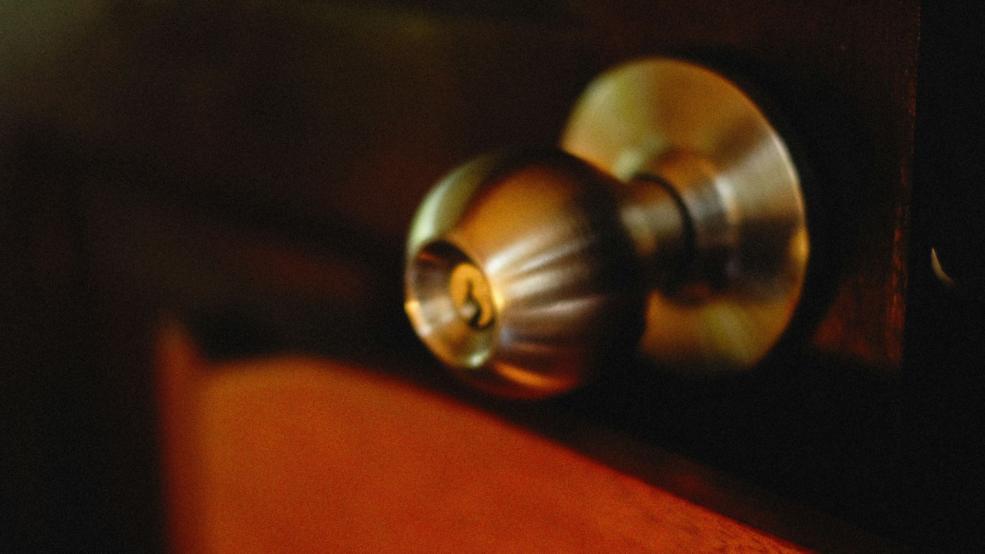 Close-up of a brass doorknob on a dark door with warm orange light below.