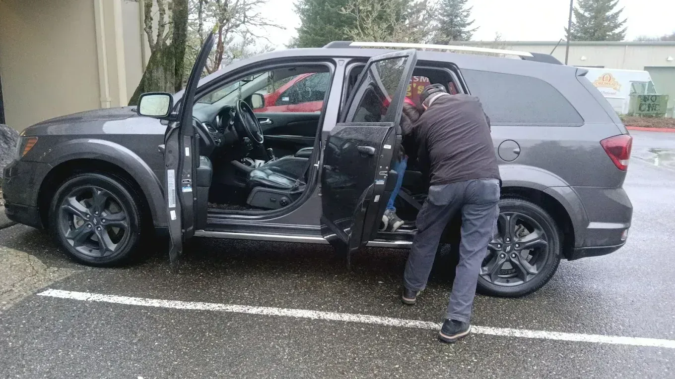 Person unloading items from a gray SUV in a rainy parking lot with the doors open