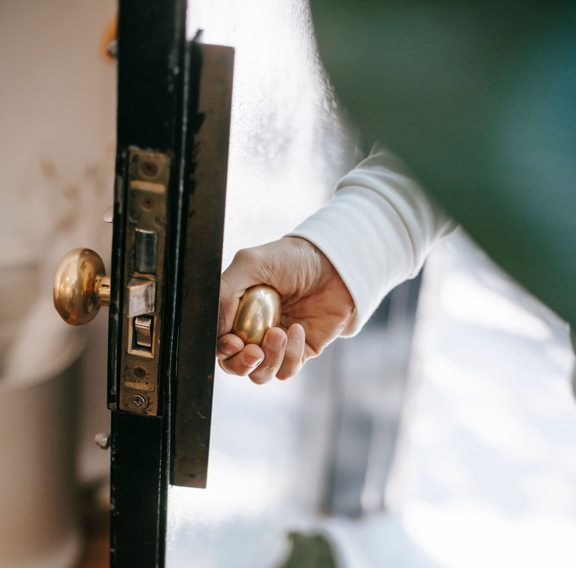 Hand opening a brass doorknob on a partially open door