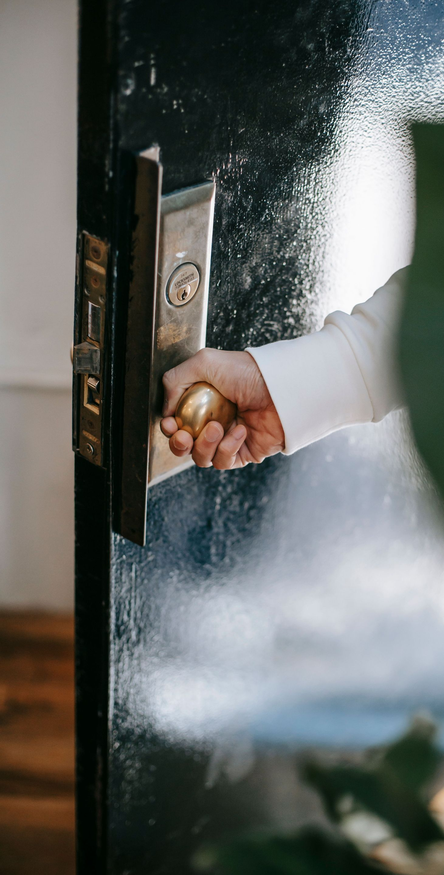 Hand turning a brass door handle to open a dark-framed glass door