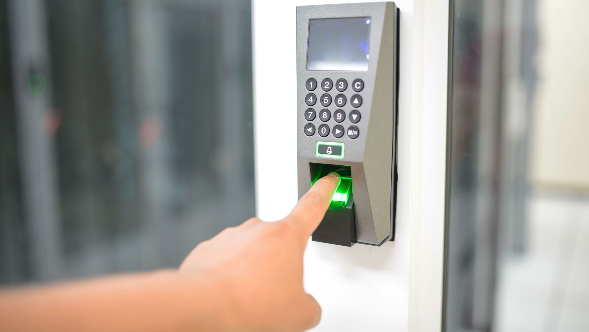 Finger pressing green-lit keypad on a wall-mounted access control device