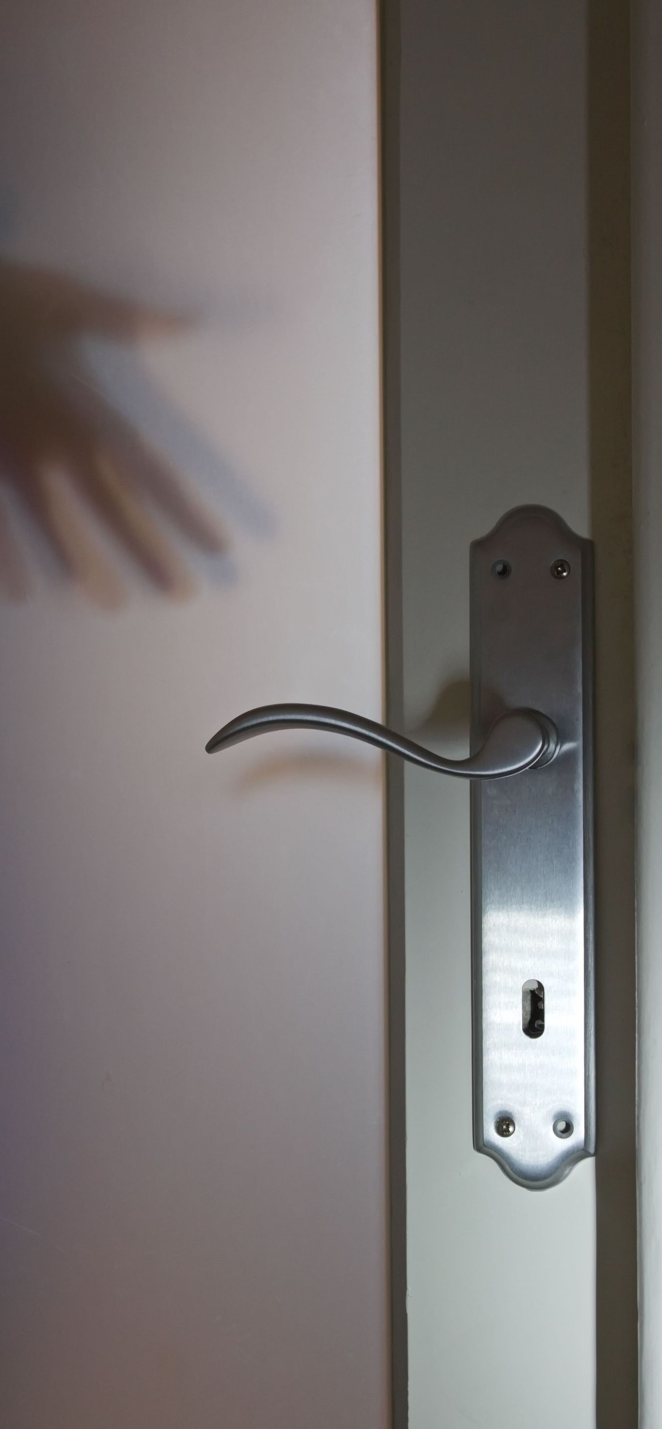 Close-up of a door handle on a white door, with a hand reaching toward it.