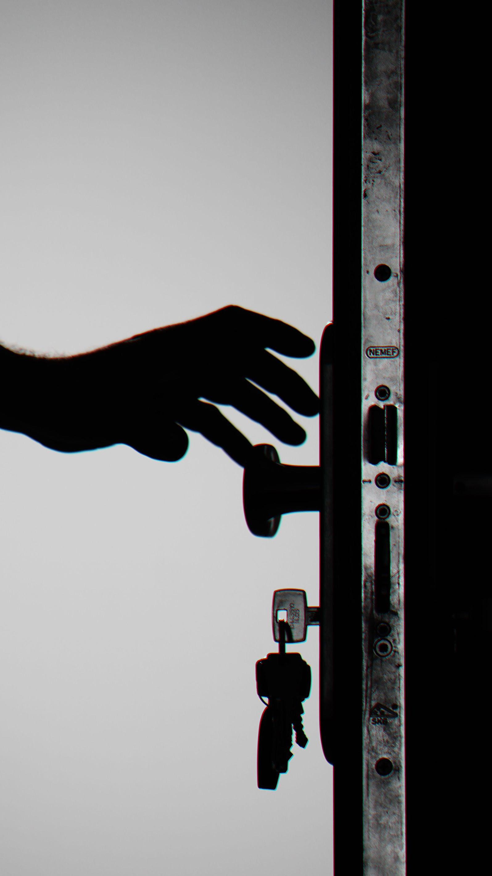 Silhouette of a hand reaching toward a door lock with keys hanging below.