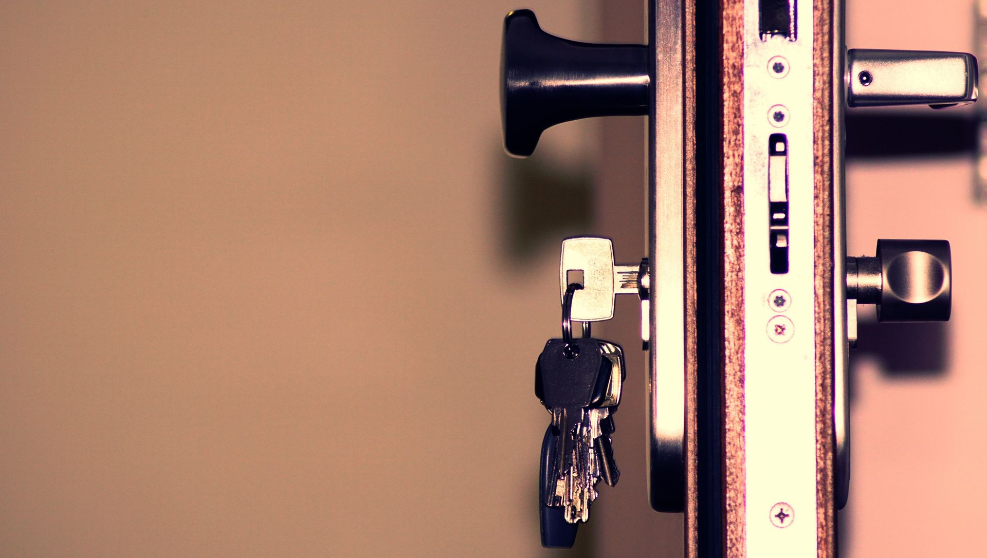 Close-up of a door lock with keys hanging from it on a beige wall