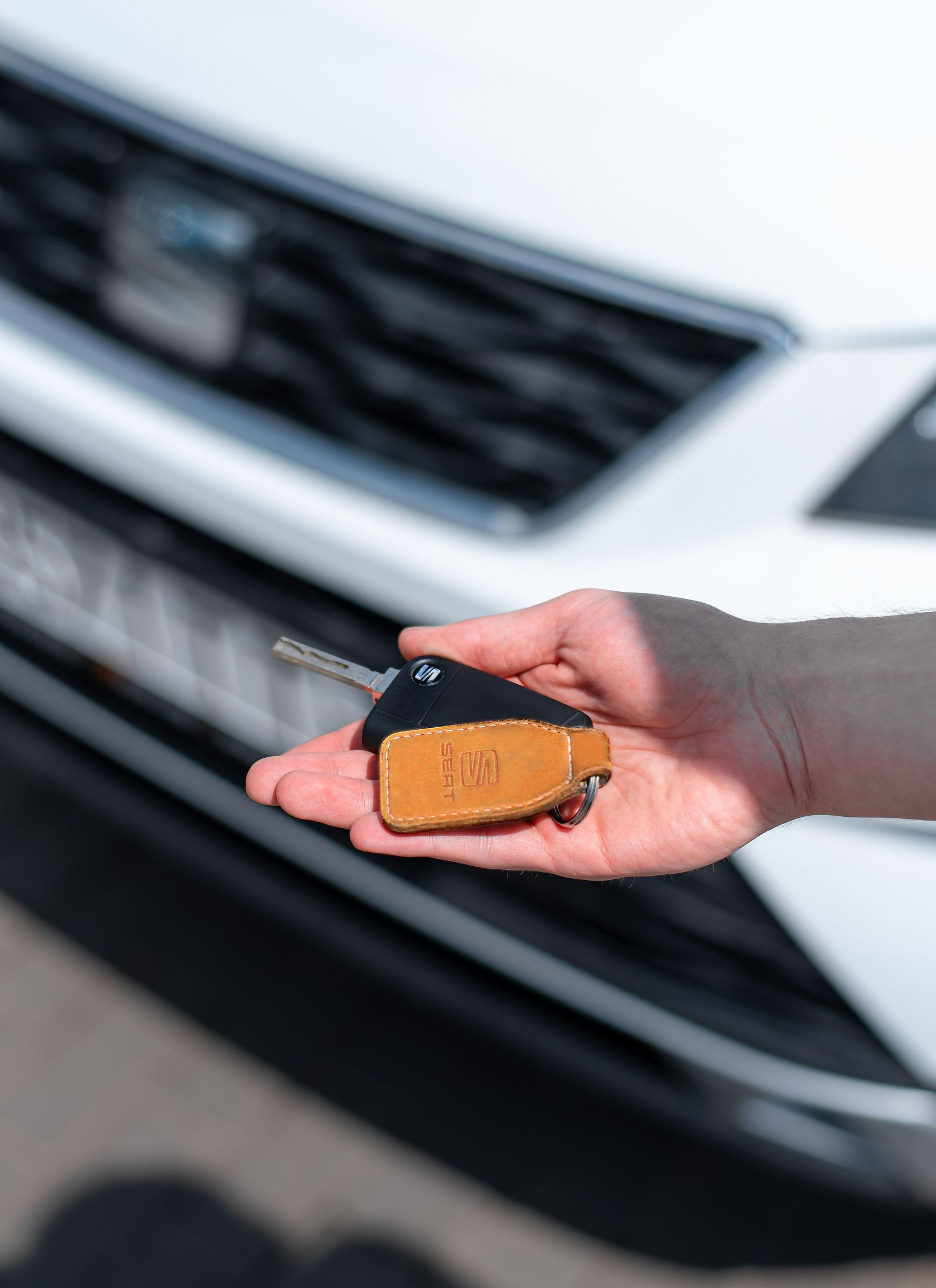 Hand holding a black-and-amber car key fob in front of a white car grille