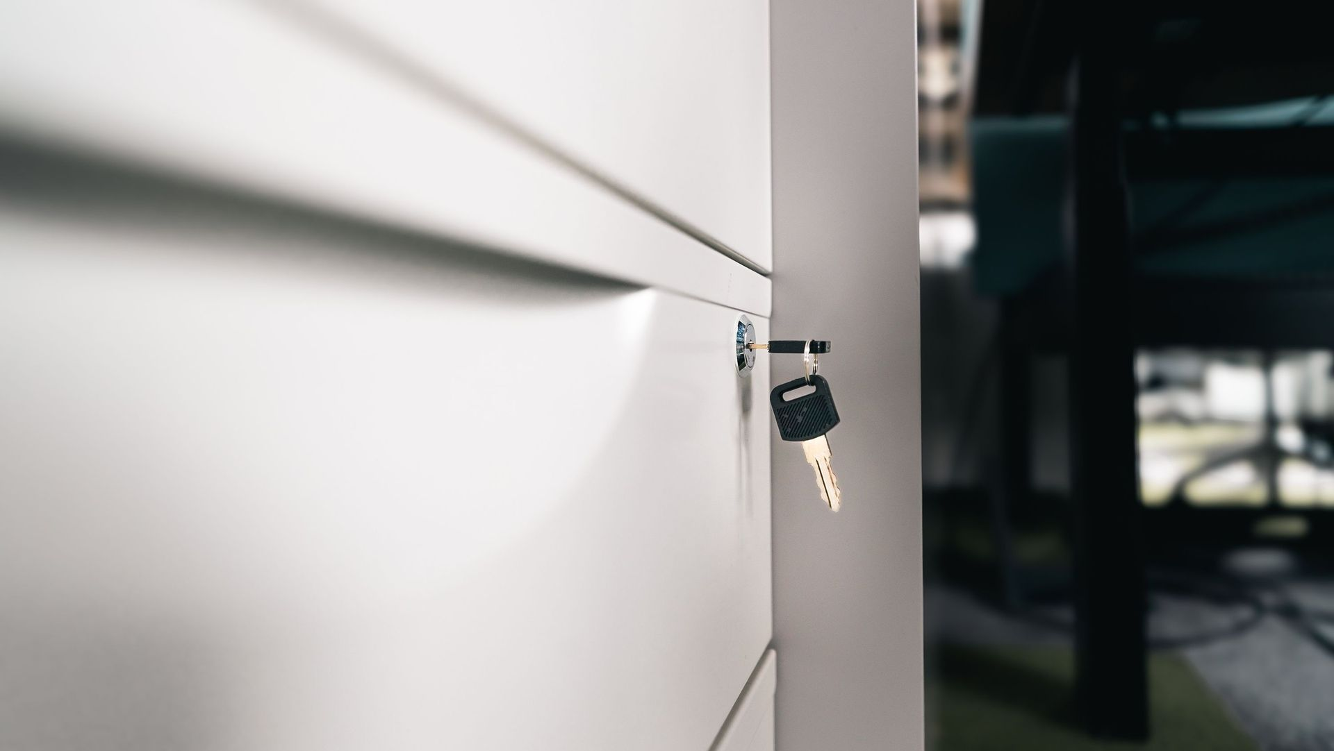 Keys in a lock on a white cabinet door near a dark doorway.
