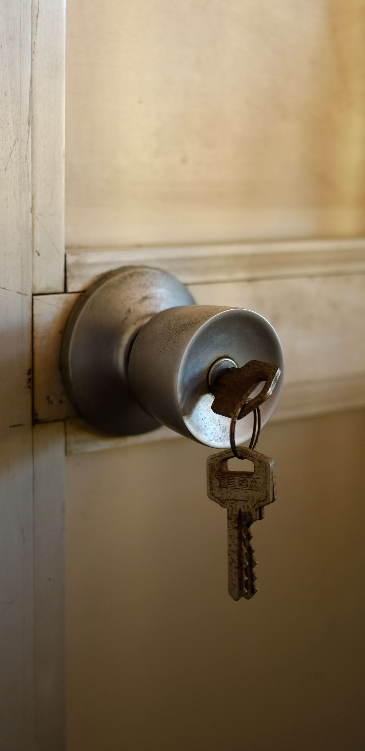Close-up of a silver door lock with a key inserted, hanging from a beige door.