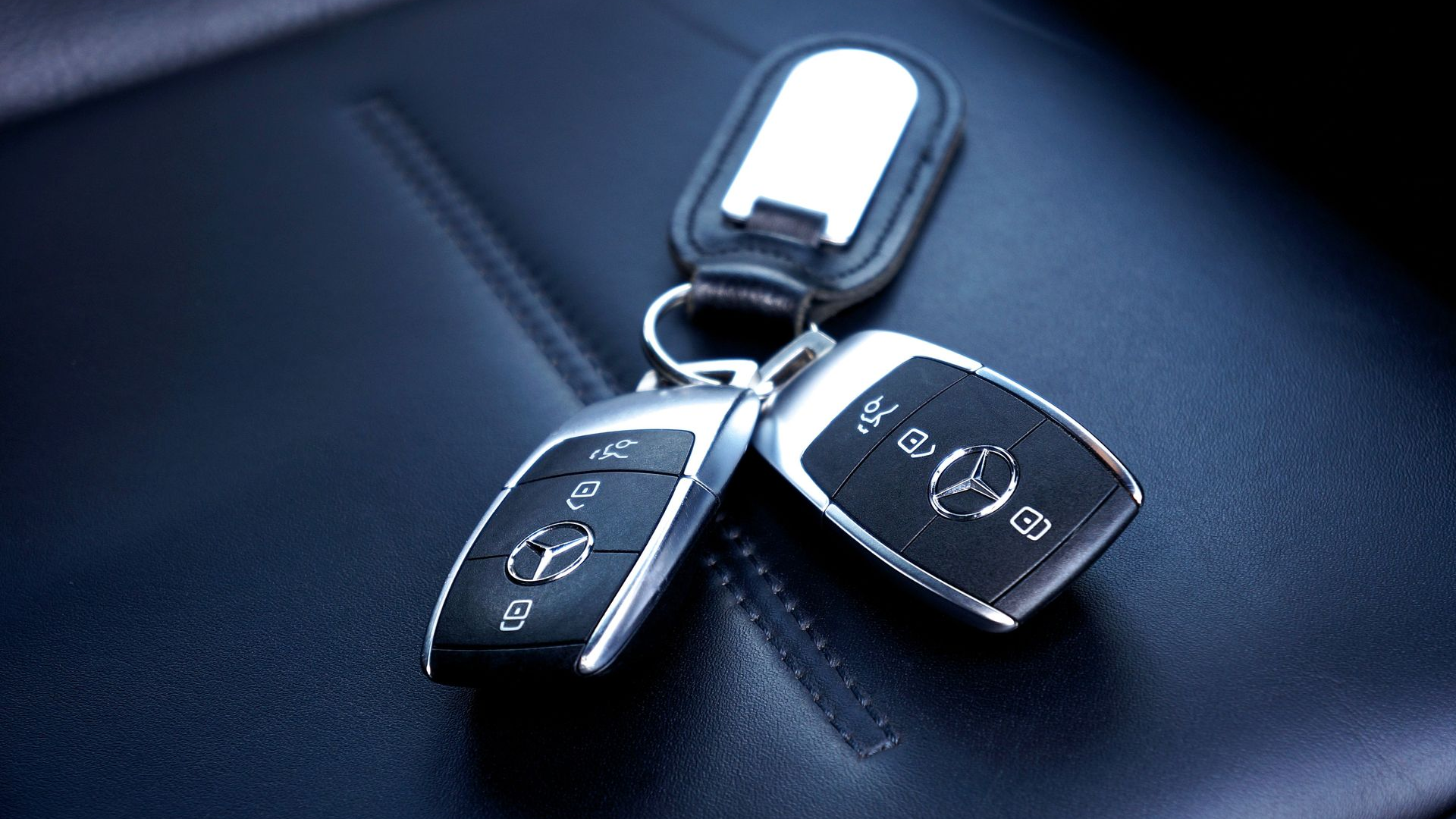 Car keys on a dark leather car seat, with a silver key fob and black remote fobs