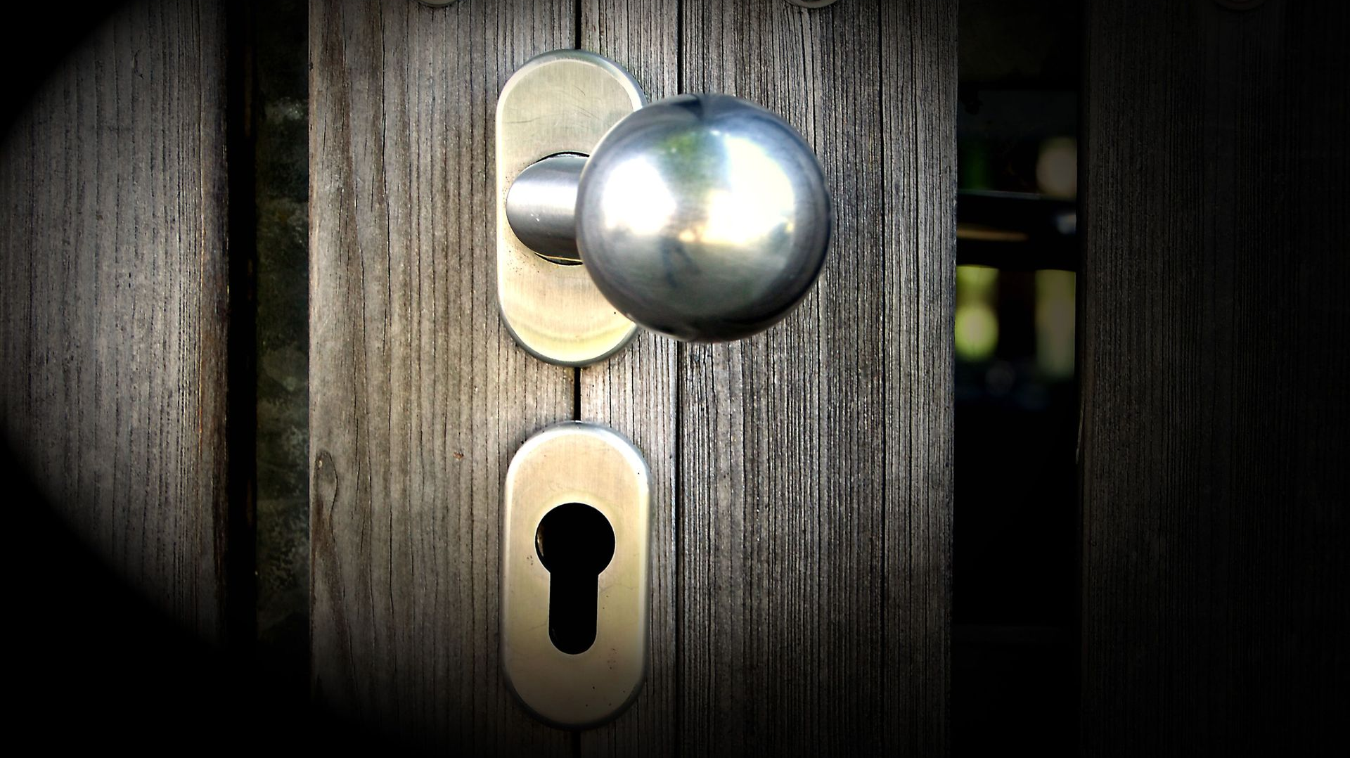 Close-up of a shiny doorknob and keyhole on a dark wooden door.