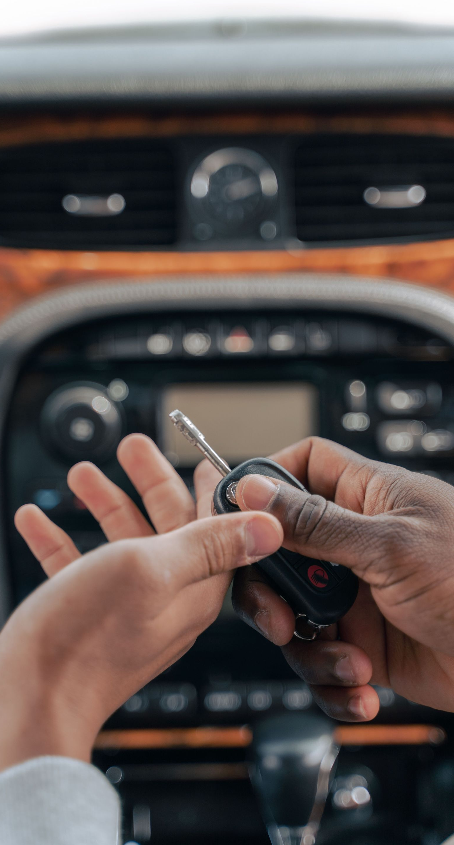 Hands holding a car key fob in front of a vehicle dashboard and center console