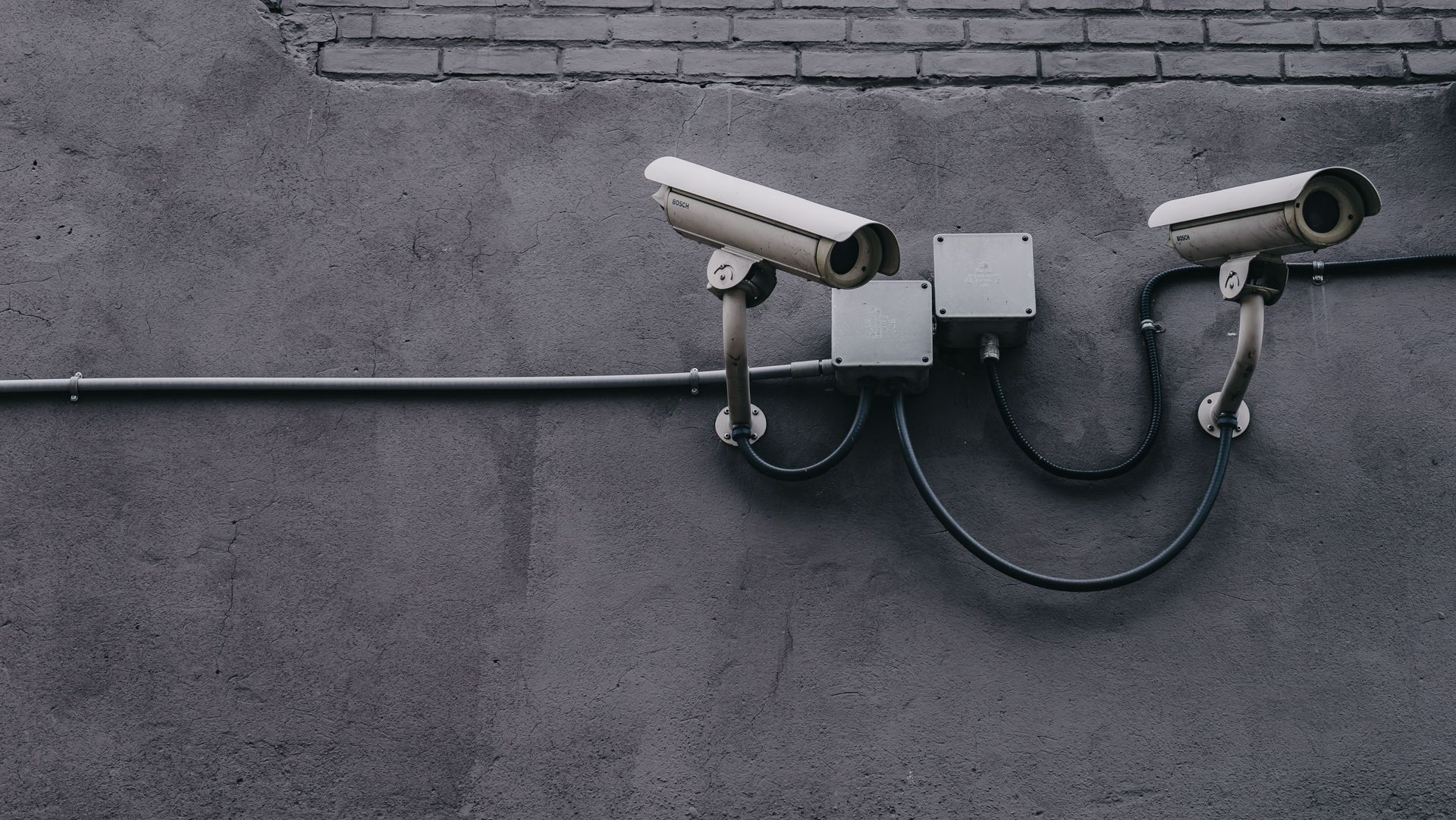 Two white security cameras mounted on a gray concrete wall with exposed cables