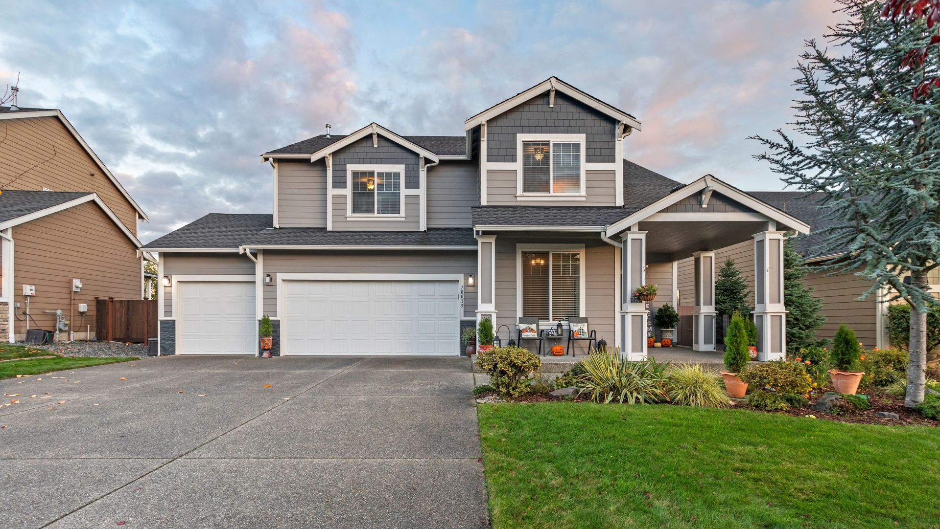 Two-story suburban house with three-car garage, covered porch, and manicured front lawn at dusk