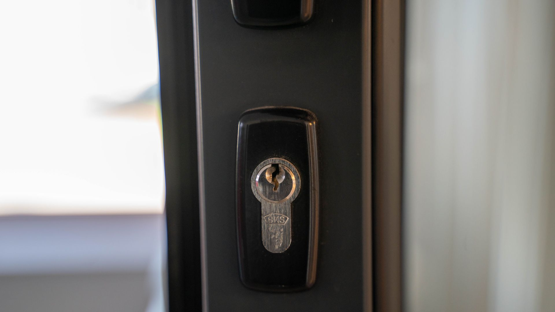 Close-up of a silver door lock on a dark handle against a blurred light background