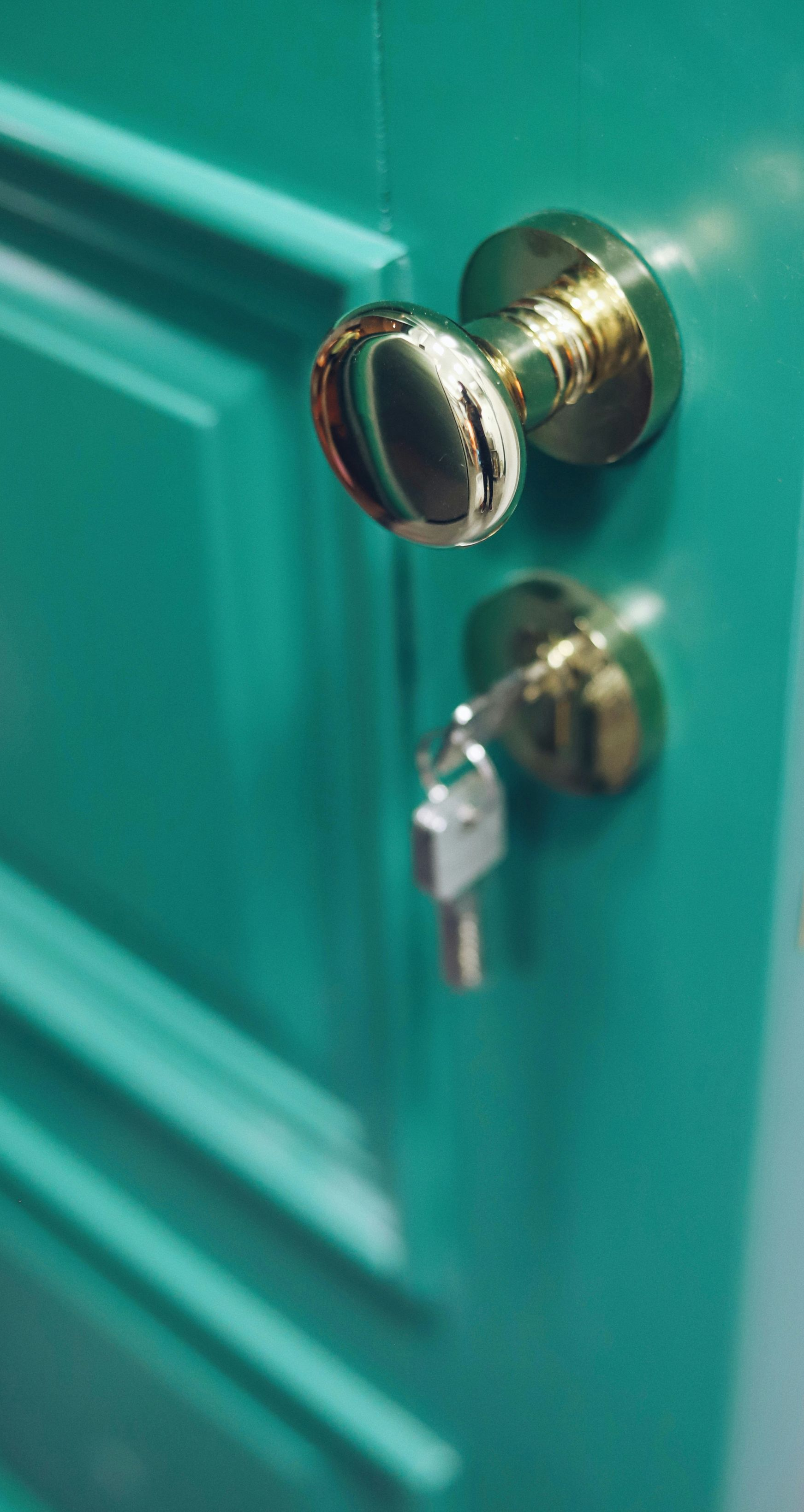 Close-up of a teal door with a brass knob and key in the lock